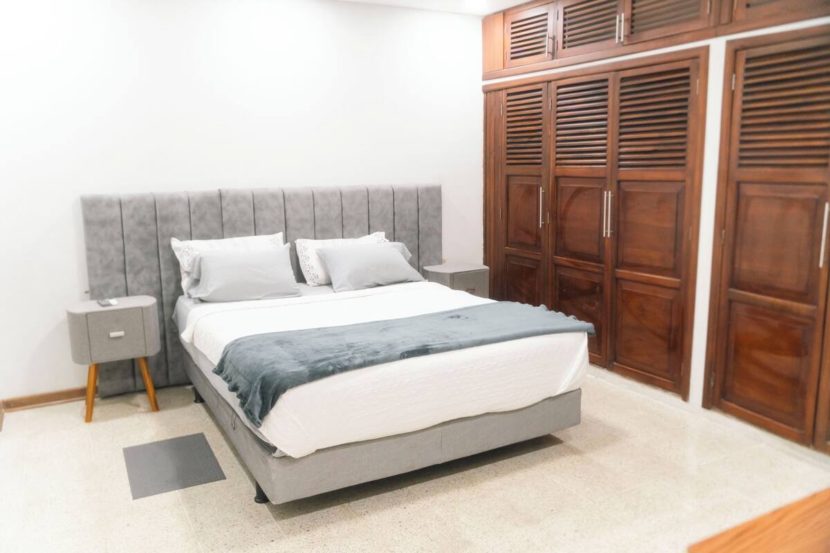 A bedroom with a bed, nightstands, a wardrobe, and a grey headboard.
