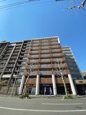 A multi-story building with balconies, a central entrance, and a sign indicating a hotel.
