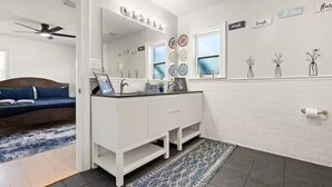 A modern bathroom with a white vanity, a large mirror, and decorative wall art. - Anastasia Island Retreat (St. Augustine)