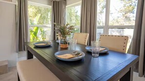 A dining table set for four with plates, cutlery, and glasses, in a room with large windows and curtains. - Anastasia Island Retreat (St. Augustine)