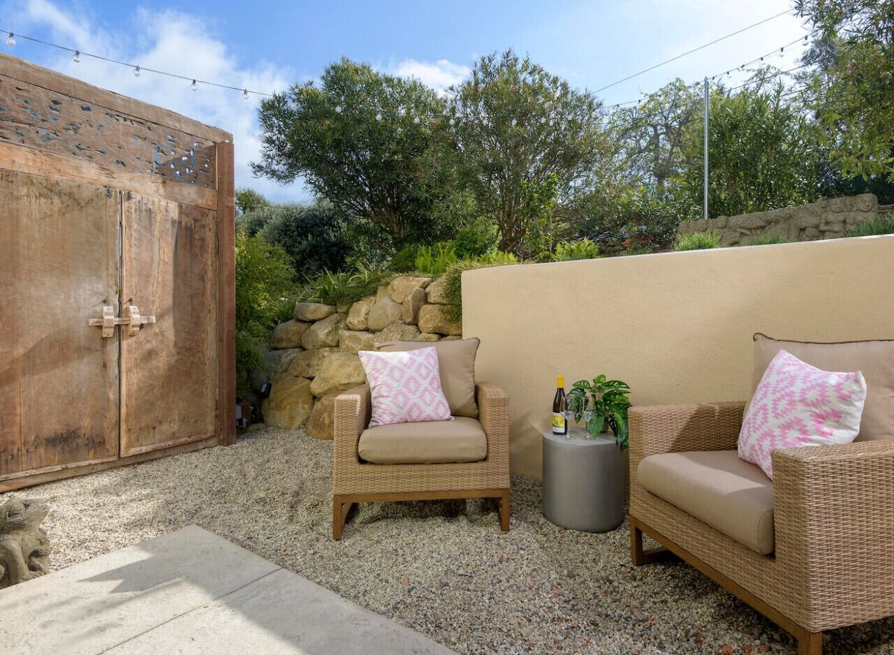 An outdoor seating area with wicker furniture, a stone wall, and a wooden gate.