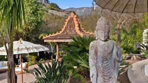 En Buddha-staty i en trädgård med en traditionell takkonstruktion och parasoller.