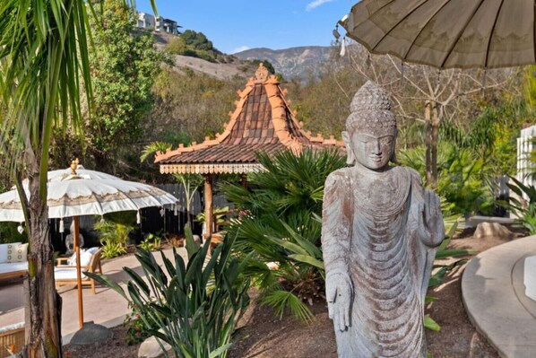 A Buddha statue in a garden with a traditional roof structure and umbrellas.