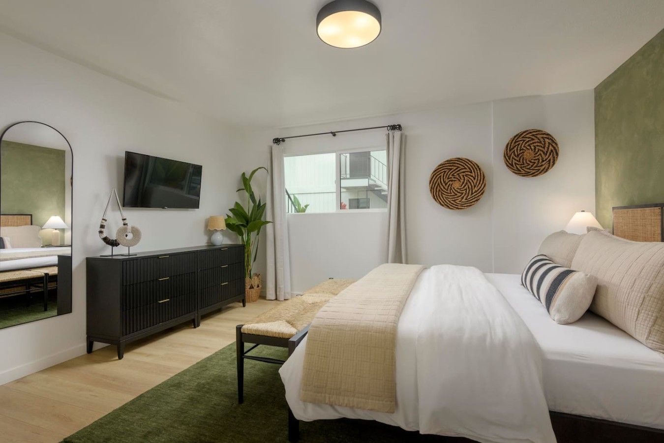 A modern bedroom with a bed, a TV, a dresser, and a large window.