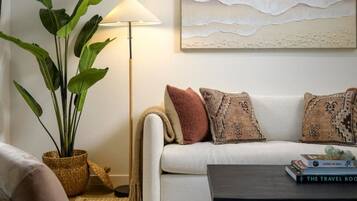 Een woonkamer met een bank, een salontafel, een lamp, een plant en een kunstwerk aan de muur.