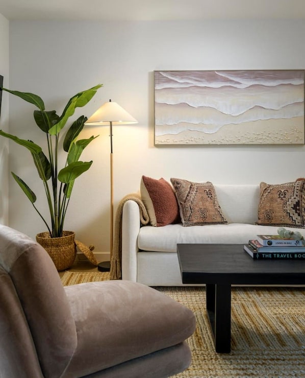 A living room with a sofa, a coffee table, a lamp, a plant, and a wall-mounted artwork.