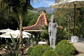 A statue in a garden with a traditional roof structure and umbrellas.