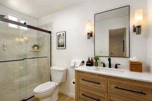 Un baño moderno con cabina de ducha de vidrio, inodoro blanco, tocador con espejo y armarios de madera.