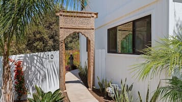 A pathway leading to a building with a decorative archway, a white fence, and various plants.