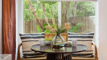 A room with a wooden bench, a round table, and a window with a view of greenery.
