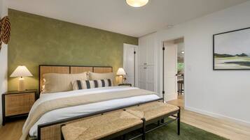 A bedroom with a bed, bedside lamps, a bench, a green wall, and a door leading to another room.