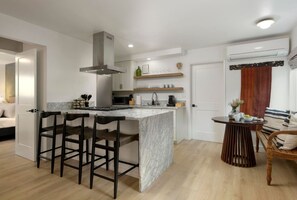 A modern kitchen with a marble island, bar stools, and a dining area with a wooden table and chairs.