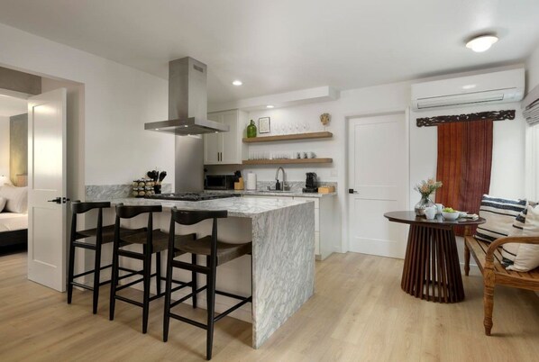Una cocina moderna con una isla de mármol, taburetes de bar y un comedor con mesa y sillas de madera.