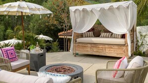 An outdoor seating area with a cushioned bench, wicker chairs, and a fire pit. - Private Garden | Family Friendly (Summerland)