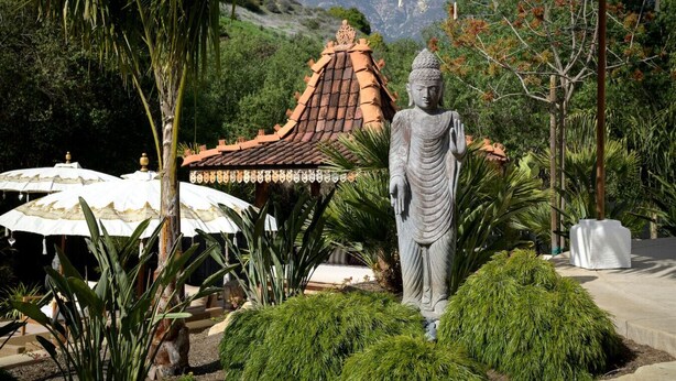 A Buddha statue in a garden with a traditional roof structure and white umbrellas. - Private Garden | Family Friendly (Summerland)