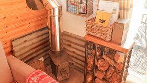 A cozy room with a wood-burning stove, a wicker basket with a book, and a wooden bench. - Cabanau Bach (Caerphilly)