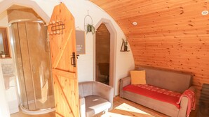A cozy cabin interior with a wooden ceiling, a glass shower enclosure, a sofa, and a small table. - Cabanau Bach (Caerphilly)