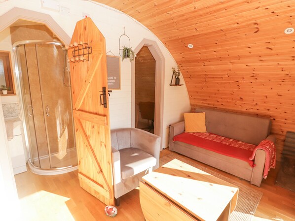 A cozy cabin interior with a wooden ceiling, a glass shower enclosure, a sofa, and a small table.
