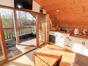 A cozy cabin with a wooden interior, a sliding glass door leading to a deck, a small kitchenette, and a dining area.