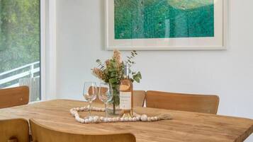 Een eetgedeelte met een houten tafel, stoelen, een hanglamp, een lijst met een schilderij en een vaas met bloemen.