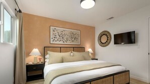 Ein modernes Schlafzimmer mit einem großen Bett, zwei Nachttischen mit Lampen, einem an der Wand montierten Fernseher und einer dekorativen Wandgestaltung.