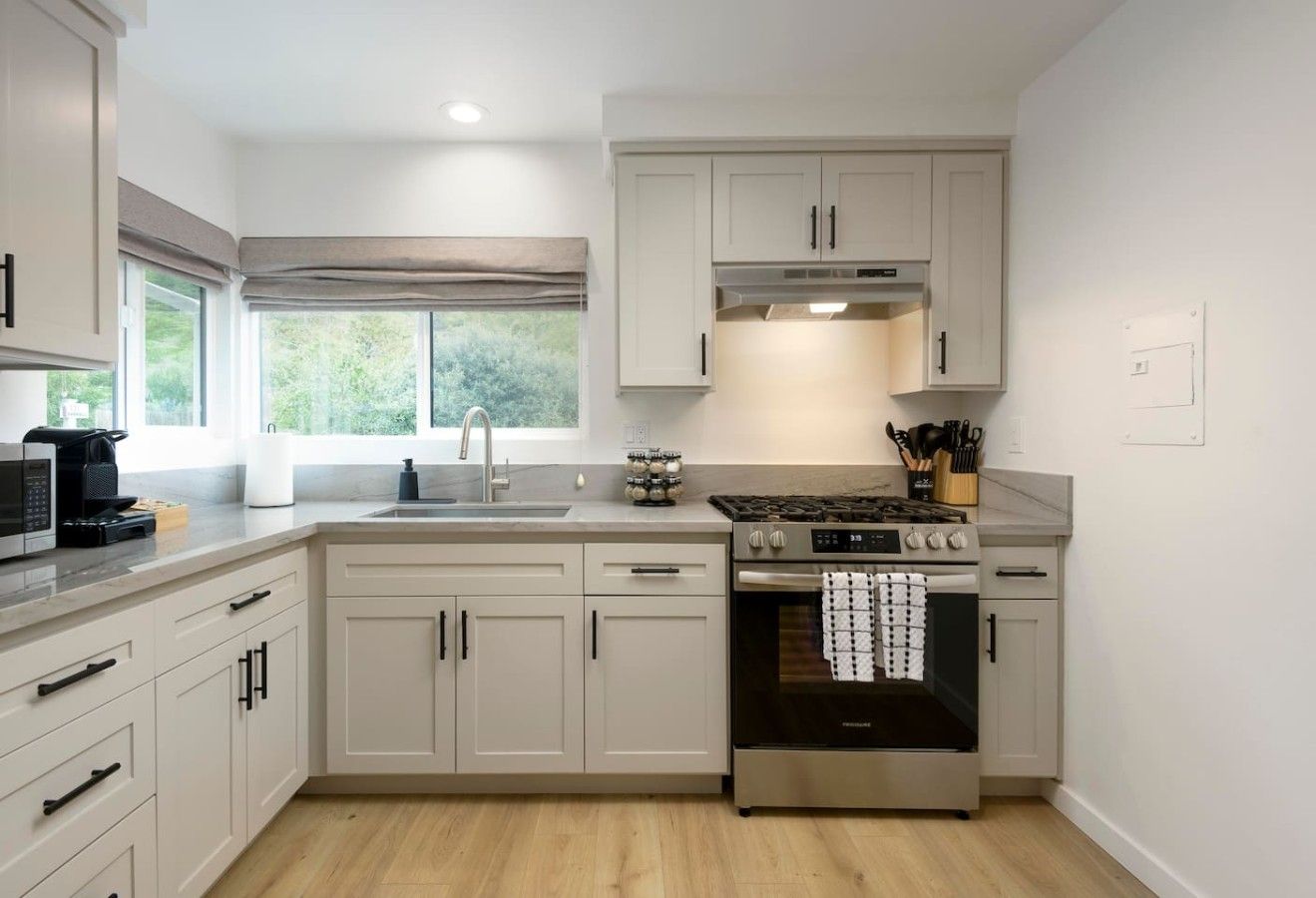 Una cocina moderna con muebles blancos, horno de acero inoxidable y ventana que proporciona luz natural.