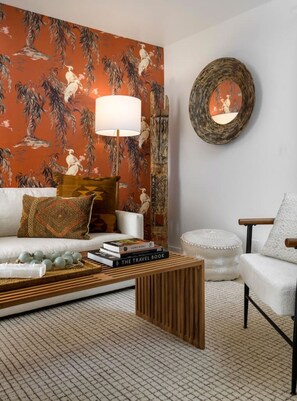 Ein Wohnzimmer mit einer Couch, einem Couchtisch, einer Lampe und einer Wand mit ornamentalem Tapetenmuster.