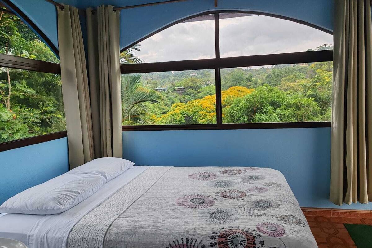 A bedroom with a large window, a bed, and curtains.