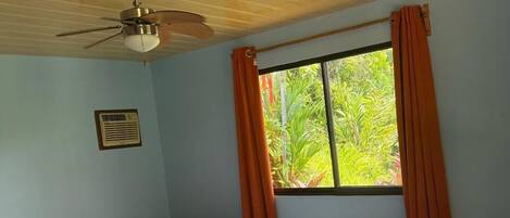 A room with two beds, a ceiling fan, a window with curtains, and a wall-mounted air conditioner.