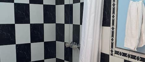 A bathroom with a checkered black and white tile wall, a white toilet, a shower with a white curtain, and a towel hanging on a rack.