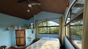Une chambre à coucher avec un lit, une fenêtre, un ventilateur de plafond et un lavabo.