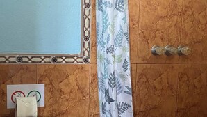 Une salle de bain équipée de toilettes, d’une poubelle, d’un rideau de douche orné d’un motif de feuilles et d’un sèche-mains.