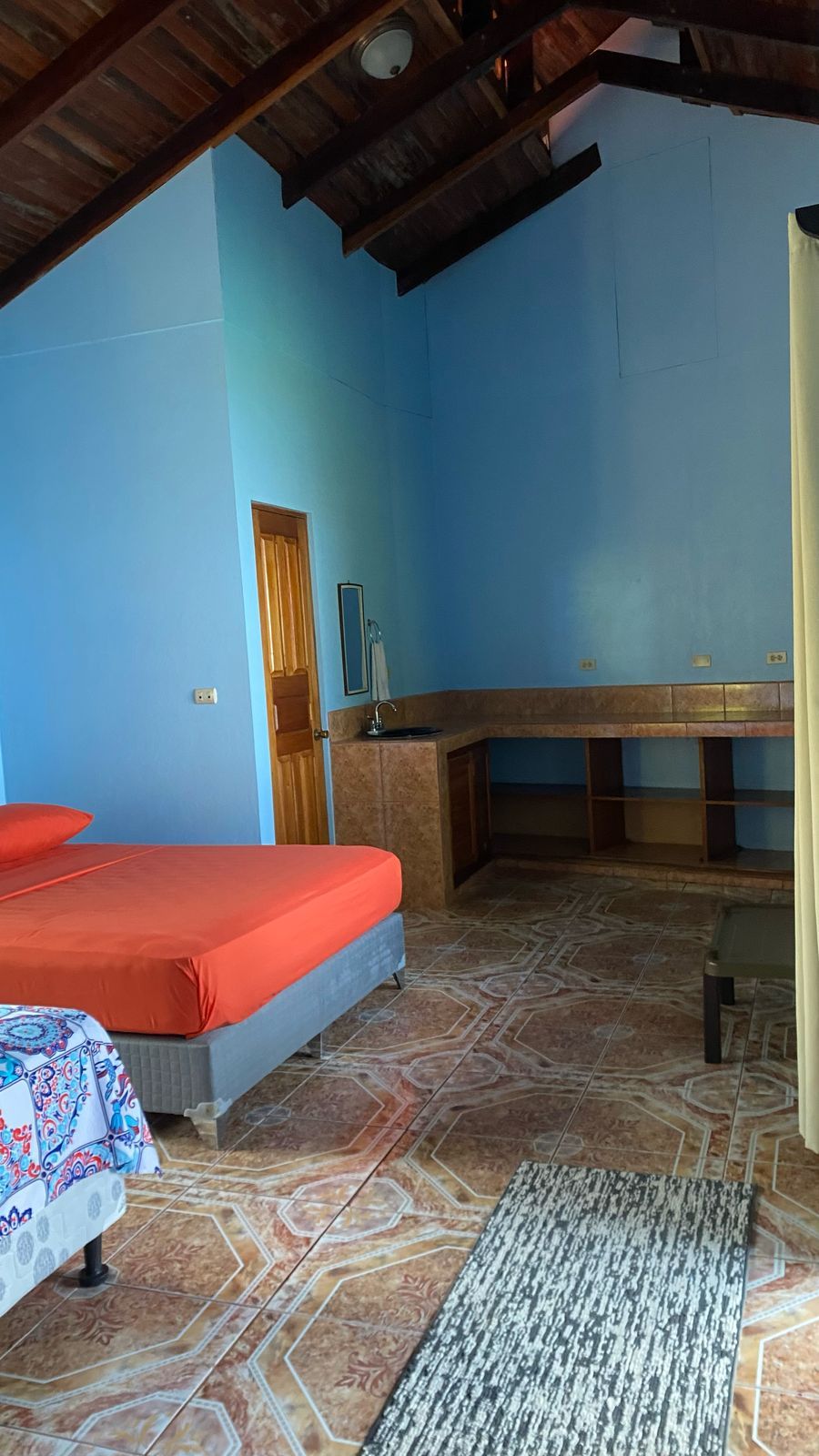 Une pièce comprenant un lit, un banc, un lavabo et une porte.