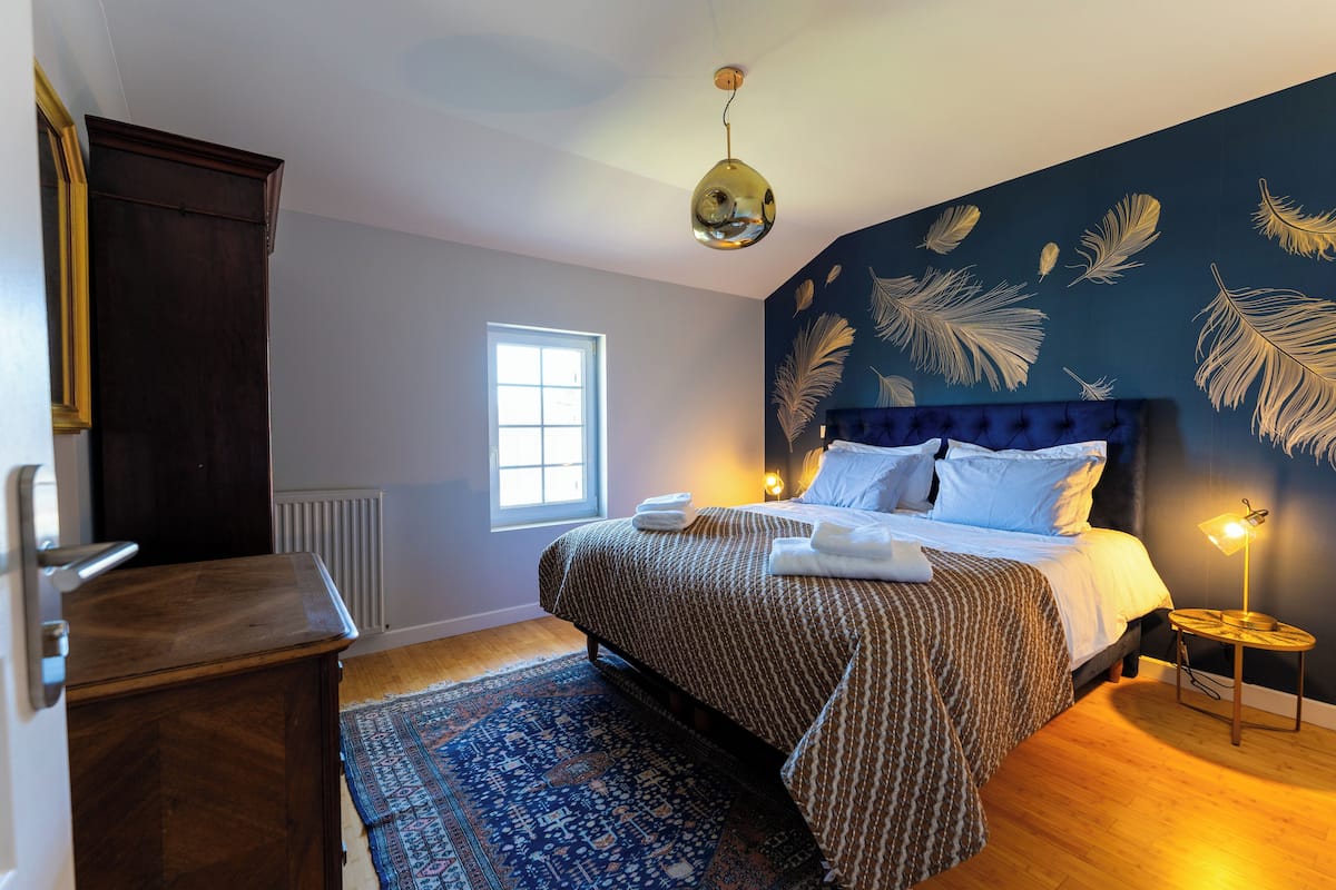 A bedroom with a large bed, a dresser, a radiator, a window, and a patterned rug.