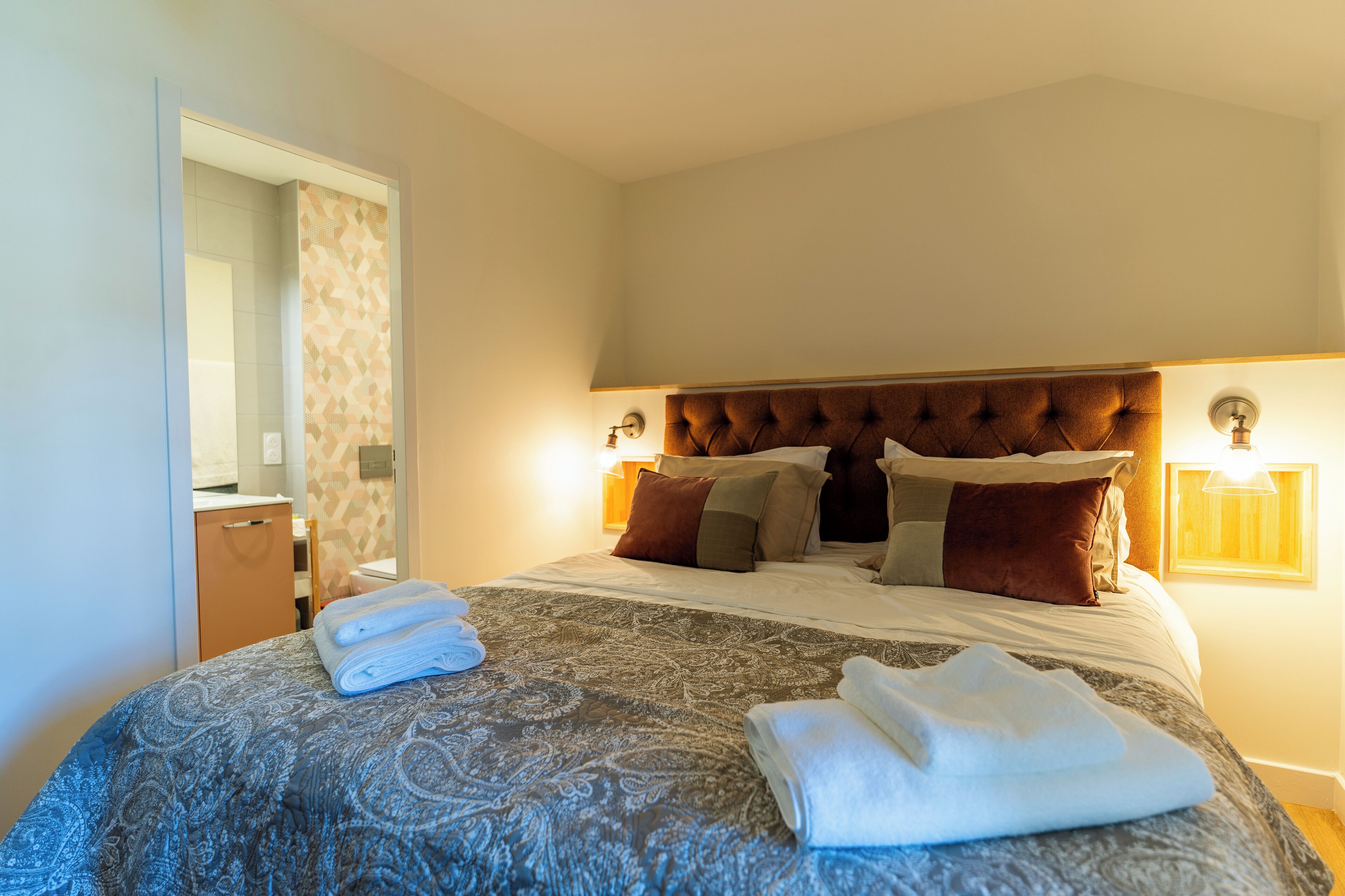 A neatly made bed with a patterned bedspread, a headboard, and several pillows.