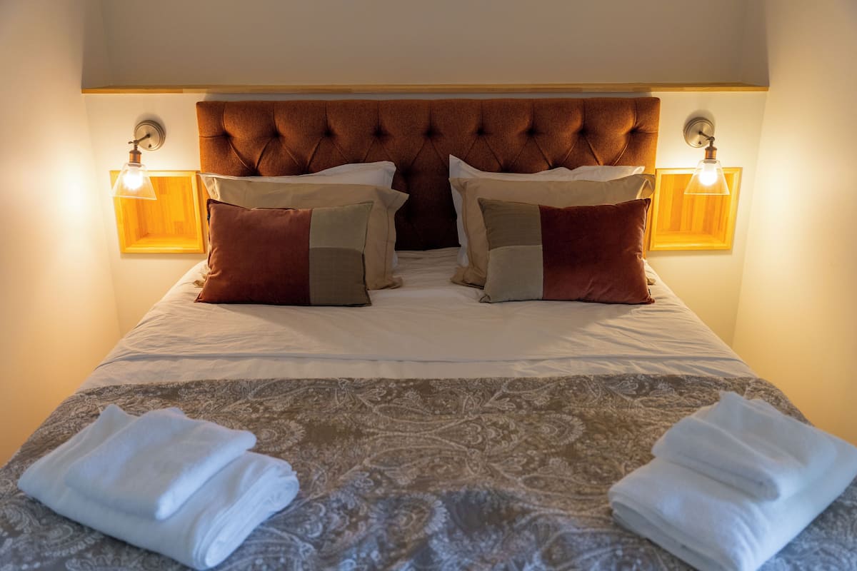 A neatly made bed with a patterned bedspread, two pillows, and two folded towels on the bed.