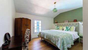 A bedroom with a bed, a wooden wardrobe, a chair, a desk, and a window.
