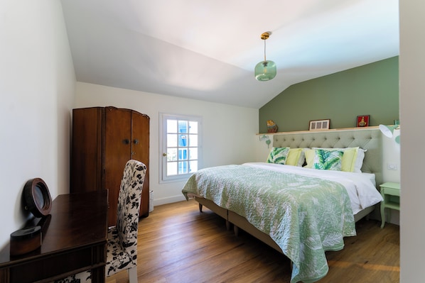 Un dormitorio con cama, un armario de madera, una silla, un escritorio y una ventana.