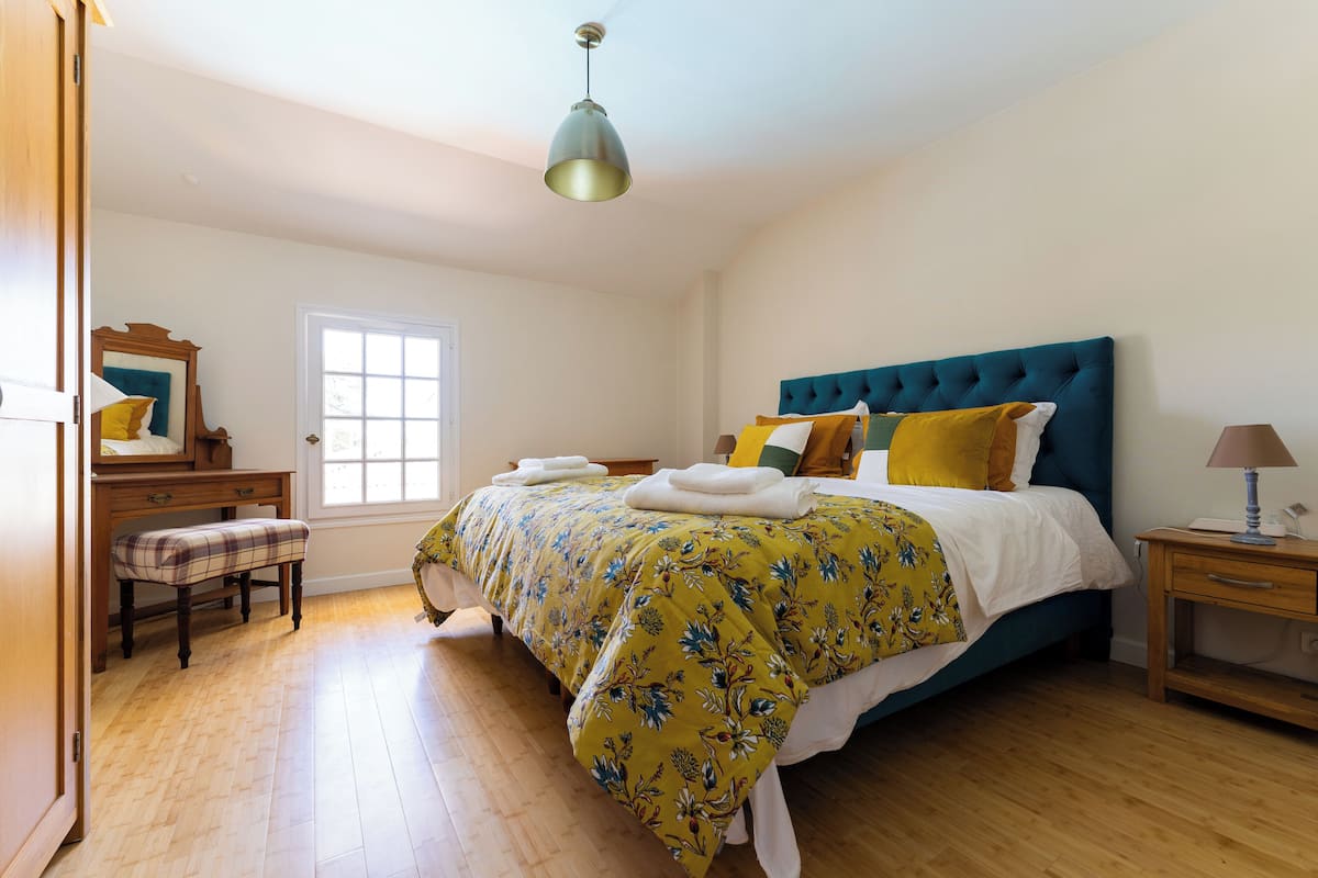 A bedroom with a bed, a bench, a bedside table, a lamp, and a window.