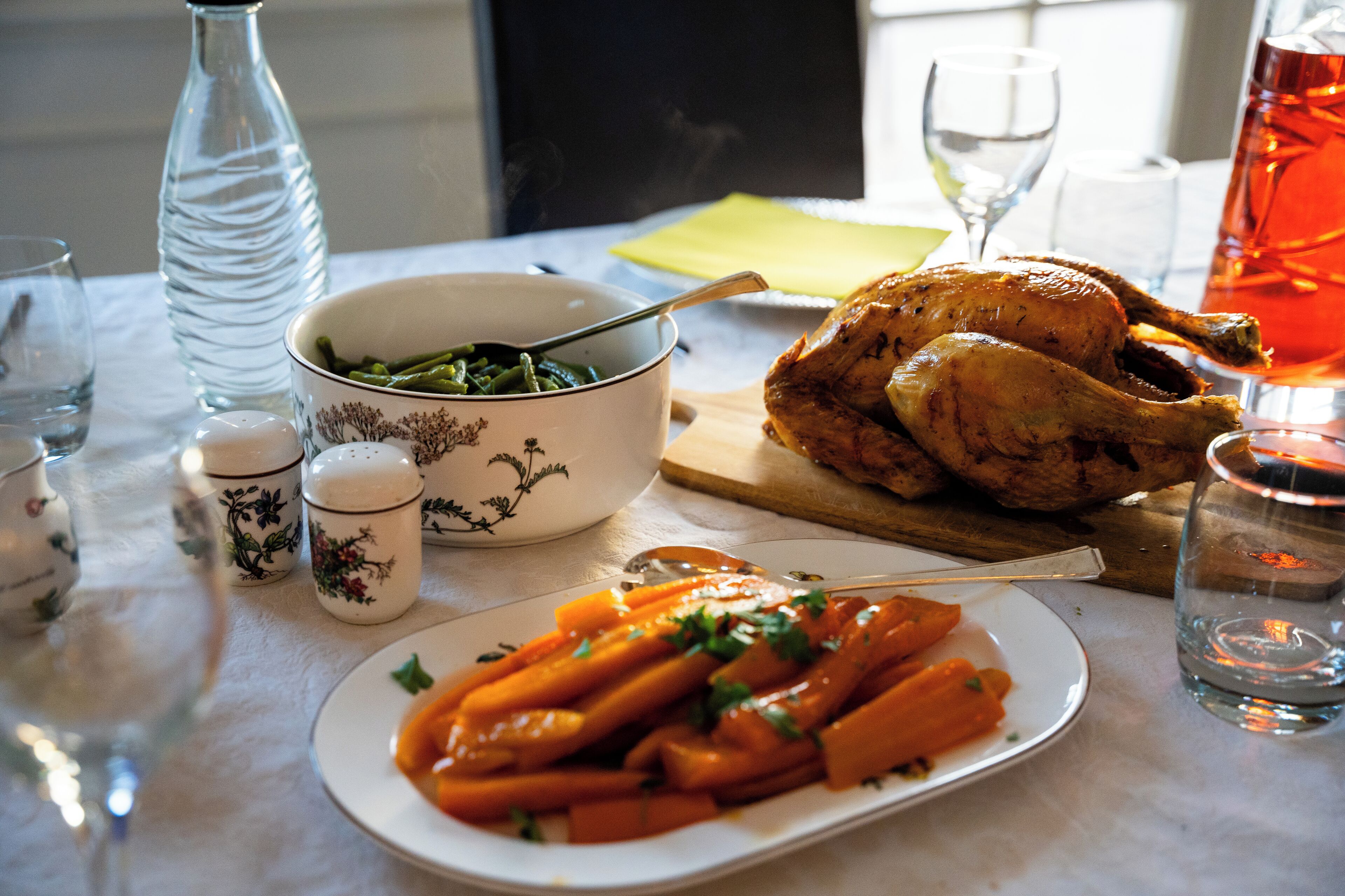 Une table à manger avec un poulet rôti, un bol de haricots verts et une assiette de carottes.