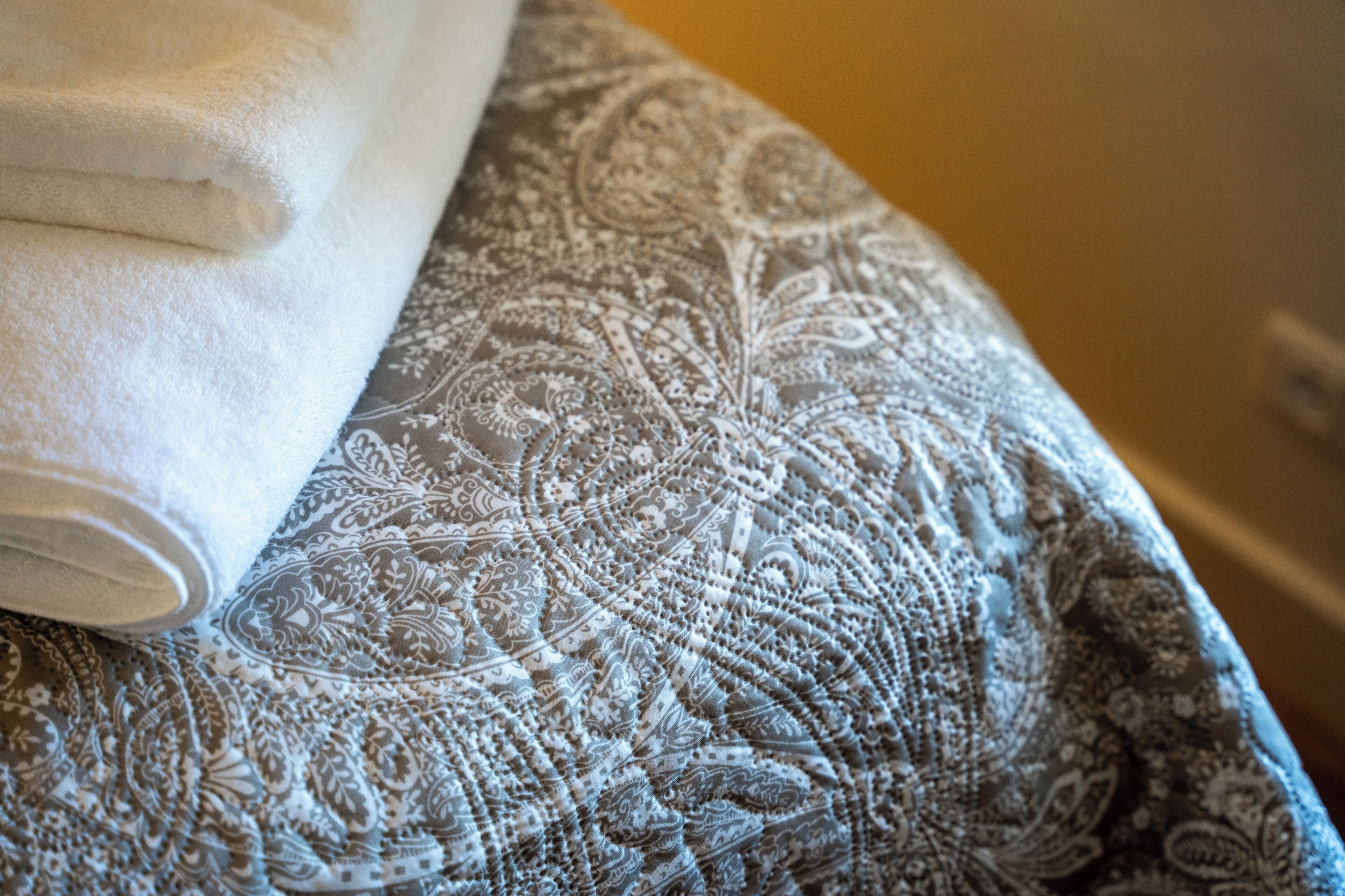 A bed with a patterned bedspread and a neatly folded white blanket.