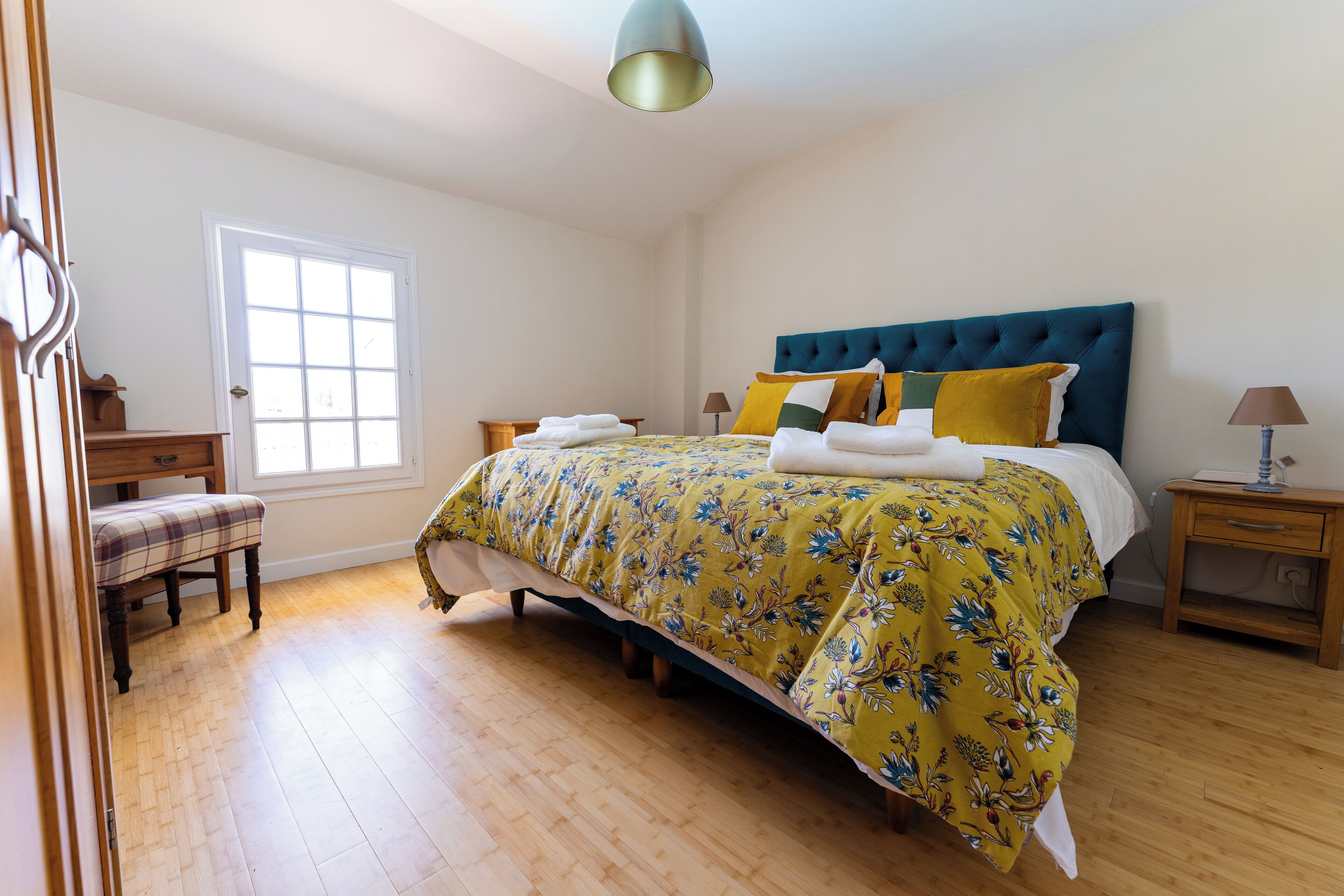 A bedroom with a bed, a bench, a bedside table, and a window.