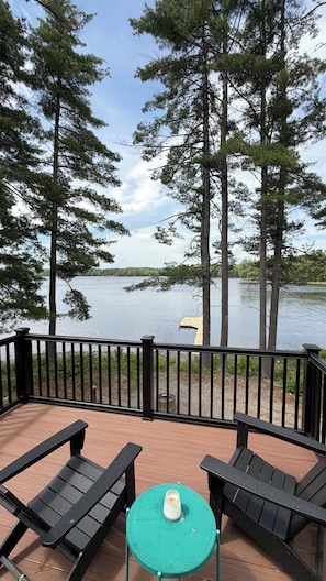 Une terrasse avec deux chaises et une petite table, donnant sur un lac bordé d’arbres et sur un quai.