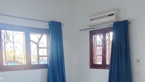 Ein Schlafzimmer mit einem Einzelbett, zwei mit Vorhängen versehenen Fenstern, einer Klimaanlage und einem Deckenventilator.