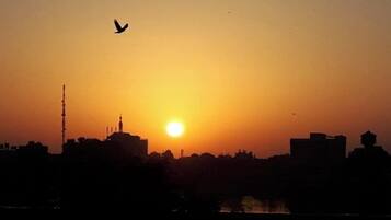 Eine Silhouette einer Stadtlandschaft bei Sonnenuntergang, mit einem Vogel am Himmel.