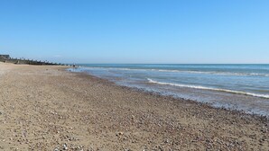 Ein Kiesstrand mit blauem Himmel und ruhiger See.