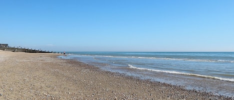 A pebbly beach with a clear sky and calm sea.