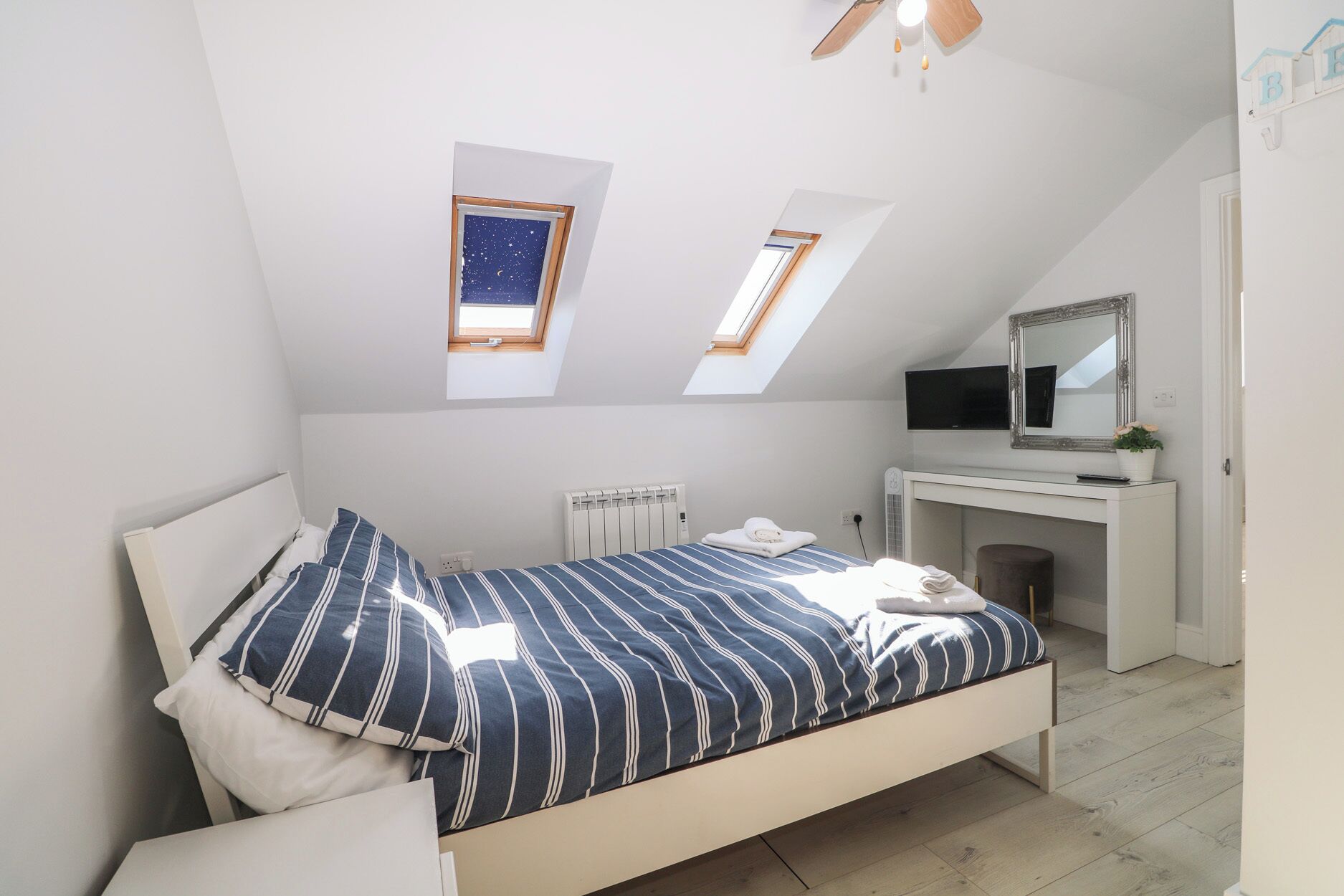 Una camera da letto con un letto, una scrivania, uno specchio e due finestre sul tetto.