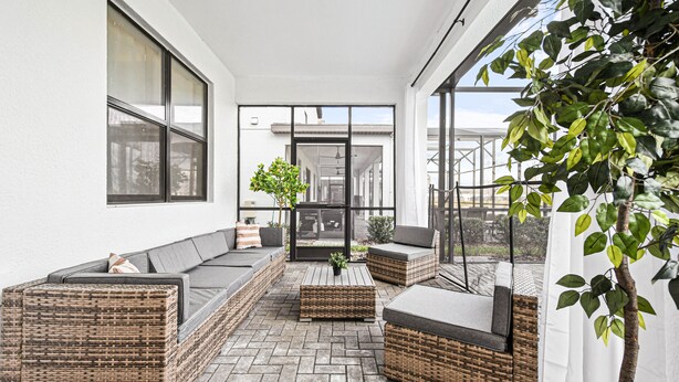 A sunlit outdoor seating area with wicker furniture, a potted plant, and a view of the building's interior. - Last Minute Disney! Private Pool, Hot Tub, Game Room & Themed Bedrooms. Book Now! #112977 (Orlando)