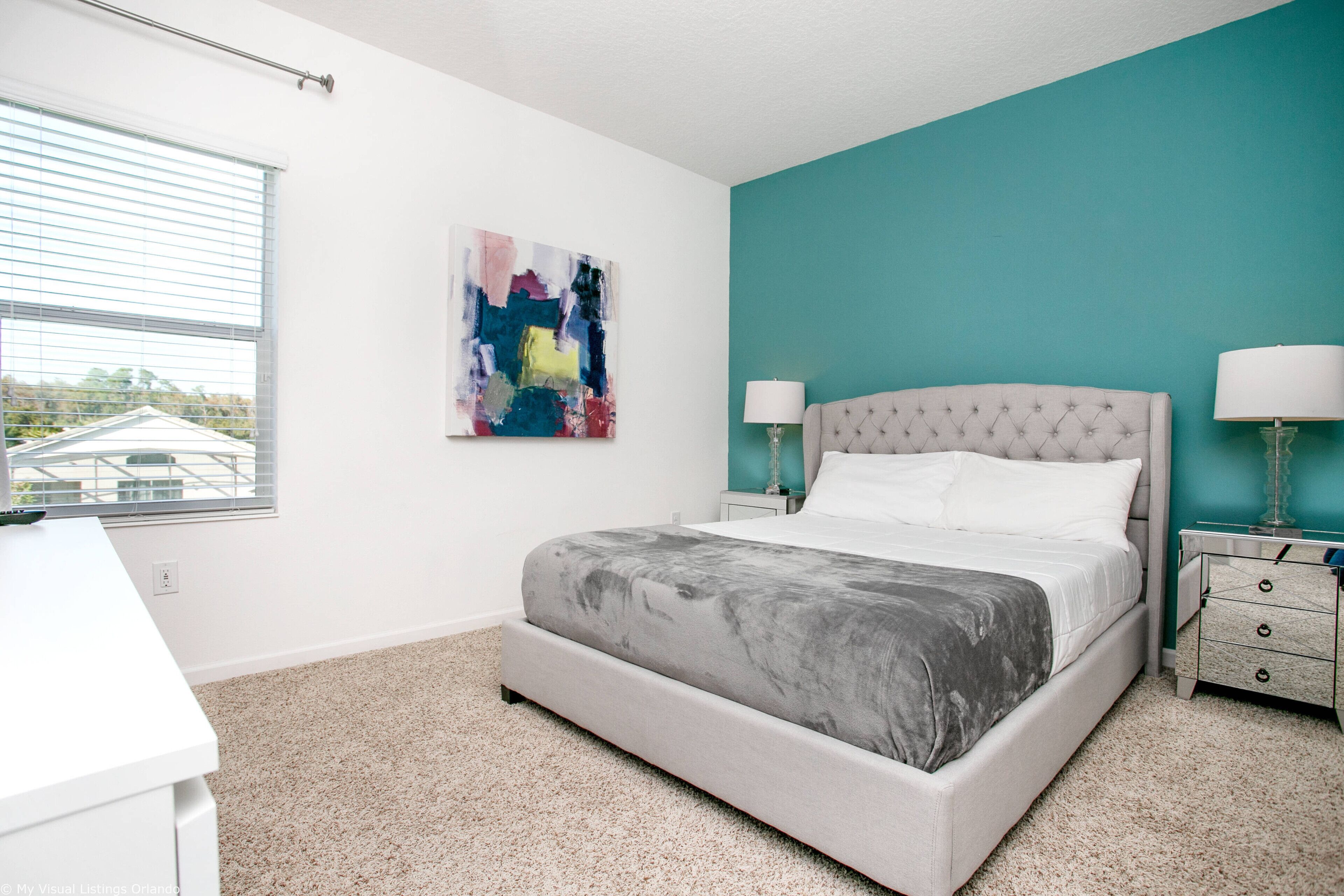 A bedroom with a bed, two bedside tables, a window, and a painting on the wall.